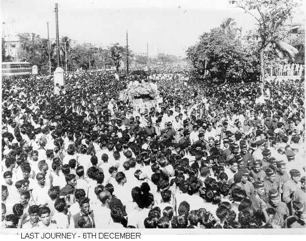 A huge crowd surrounds the flower-covered vehicle carrying Ambedkar's body during his funeral procession. The print is labelled "Last Journey – 6th December"; Wikimedia Commons dates the photograph 7 December 1956.